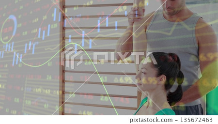 Trainer guiding stretching woman in green top on wall bars at gym, with stock chart overlay 135672463
