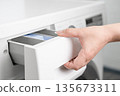 A woman's hand opens the detergent drawer in a washing machine 135673311