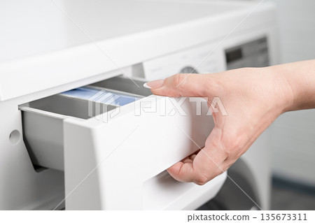 A woman's hand opens the detergent drawer in a washing machine A woman's hand opens the detergent drawer in a washing machine 135673311