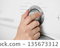 A woman's hand sets the wash cycle in a washing machine 135673312