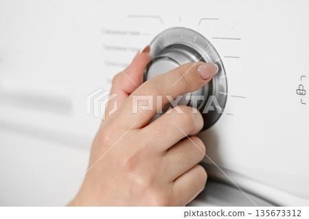A woman's hand sets the wash cycle in a washing machine 135673312
