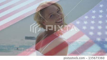 Smiling woman in strap dress looking back on shoreline, with U 135673360