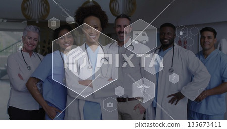 Smiling medical team in hospital hallway wearing lab coats, scrubs, stethoscopes with medical icons 135673411