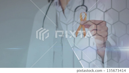Showing physician in lab coat holding gold ribbon in studio, with stethoscope and digital overlay 135673414