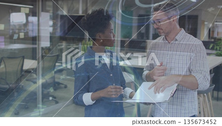 Reviewing analytics on laptop by two professionals in open plan office, digital overlay Reviewing analytics on laptop by two professionals in open plan office, digital overlay 135673452