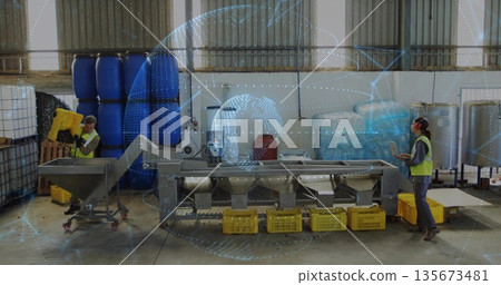 Operators monitoring tablet and lifting yellow plastic crates in warehouse, with conveyor Operators monitoring tablet and lifting yellow plastic crates in warehouse, with conveyor 135673481