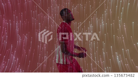 Posing fit male athlete wearing red sports uniform in studio, with glowing vertical light streaks 135673482