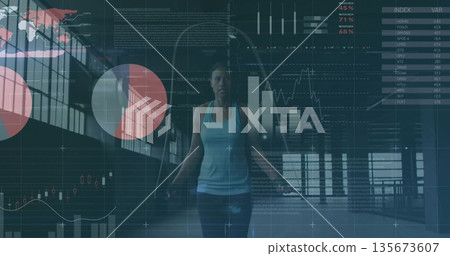 Jumping athletic woman gripping rope in gym studio, with grid windows and financial chart overlay 135673607