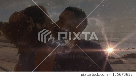 Kissing couple embracing on sandy beach at sunset, with sun flare, ocean waves and rock formations Kissing couple embracing on sandy beach at sunset, with sun flare, ocean waves and rock formations 135673632