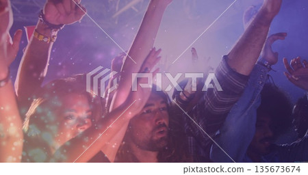 Dancing group of five concert fans celebrating under purple, pink lights amid haze and metal truss 135673674