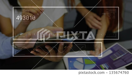 Coworkers in business attire reviewing smartphone and tablet charts in office meeting room 135674760