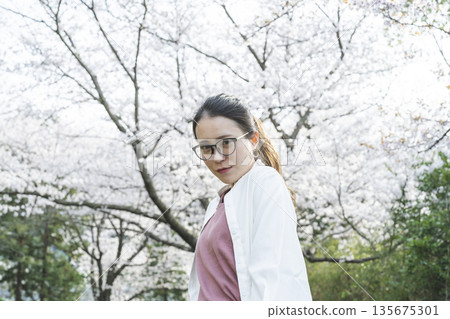 Young woman walking along cherry blossom trees Young woman walking along cherry blossom trees 135675301