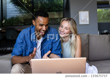 Couple enjoying video call on laptop, smiling and sitting on cozy sofa 135675737