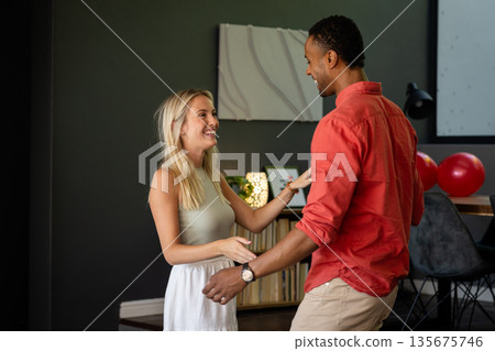 Couple dancing and smiling at home during joyful celebration with balloons Couple dancing and smiling at home during joyful celebration with balloons 135675746
