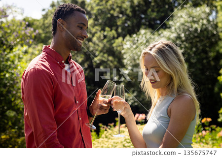 Couple celebrating outdoors, toasting with champagne glasses in sunny garden Couple celebrating outdoors, toasting with champagne glasses in sunny garden 135675747