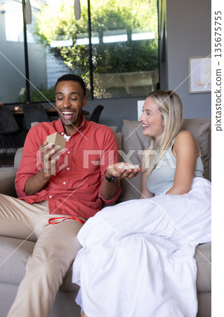 Couple exchanging gifts on cozy sofa, sharing joyful moments at home 135675755