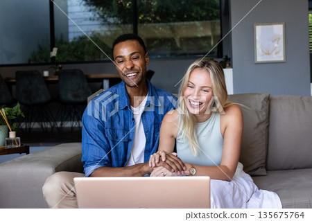 Smiling couple using laptop at home, enjoying video call together 135675764