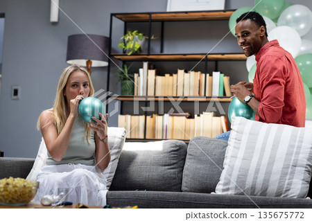 Friends preparing for celebration, inflating balloons and smiling in living room 135675772