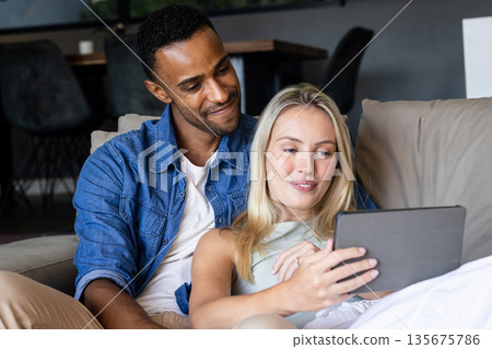 Couple relaxing on couch, enjoying tablet together at home, smiling warmly Couple relaxing on couch, enjoying tablet together at home, smiling warmly 135675786