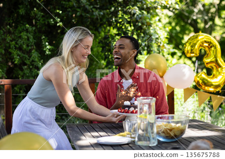 Celebrating birthday outdoors, friends sharing cake and laughter with festive decorations Celebrating birthday outdoors, friends sharing cake and laughter with festive decorations 135675788