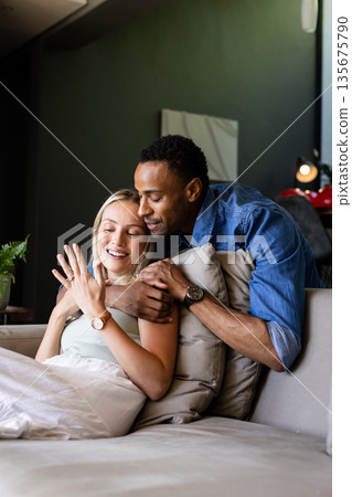Couple celebrating engagement at home, smiling and embracing on cozy sofa Couple celebrating engagement at home, smiling and embracing on cozy sofa 135675790