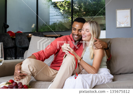 Couple exchanging gifts on sofa, smiling and enjoying cozy moment at home 135675812