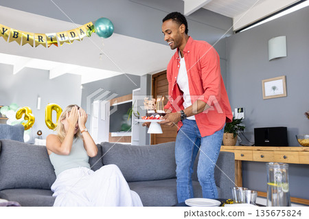 Man surprising woman with birthday cake at home, creating joyful celebration moment Man surprising woman with birthday cake at home, creating joyful celebration moment 135675824