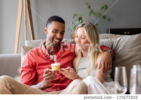 Couple celebrating birthday at home, smiling and holding cupcake with candle Couple celebrating birthday at home, smiling and holding cupcake with candle 135675828