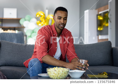 Man in red shirt enjoying snacks and drink at home during celebration Man in red shirt enjoying snacks and drink at home during celebration 135675846