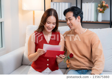 Happy asian couple sitting on sofa celebrating Valentine's Day with romantic surprise together. 135675860