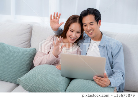 Happy asian couple video call on laptop together in living room at home. Happy asian couple video call on laptop together in living room at home. 135675879