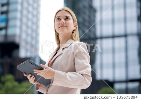 Young caucasian businesswoman reading on digital tablet outdoors in city. Young caucasian businesswoman reading on digital tablet outdoors in city. 135675894