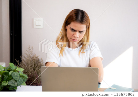 Unhappy young caucasian businesswoman using laptop computer on desk with stress and burnout. 135675902