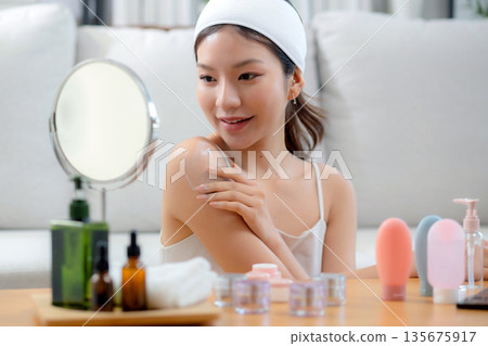Beauty young asian woman applying cream or lotion while looking mirror in living room. 135675917