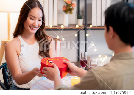 Romantic asian man giving heart shape gift box to girlfriend, surprise for Valentine's Day. 135675934