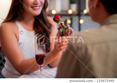 Romantic asian man giving rose to smiling woman during dinner, surprise gift for Valentine's Day. Romantic asian man giving rose to smiling woman during dinner, surprise gift for Valentine's Day. 135675940