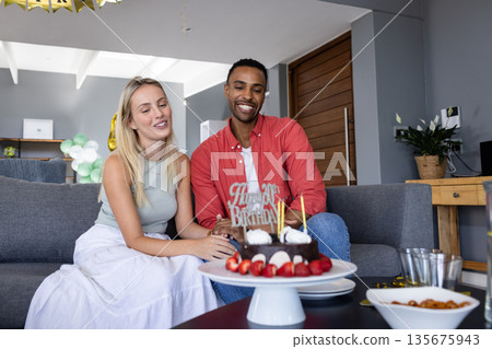 Couple celebrating birthday at home with cake and joyful smiles Couple celebrating birthday at home with cake and joyful smiles 135675943
