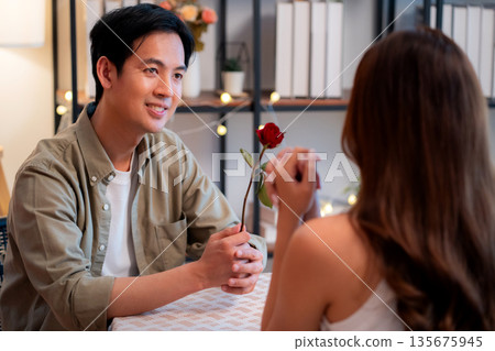 Romantic asian man giving rose to woman during dinner, surprise gift for Valentine's Day. 135675945