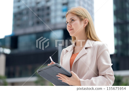 Young caucasian businesswoman writing on digital tablet in city. 135675954