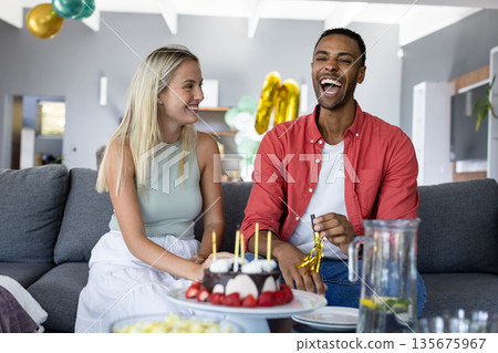 Friends celebrating birthday at home, laughing and enjoying cake with candles 135675967