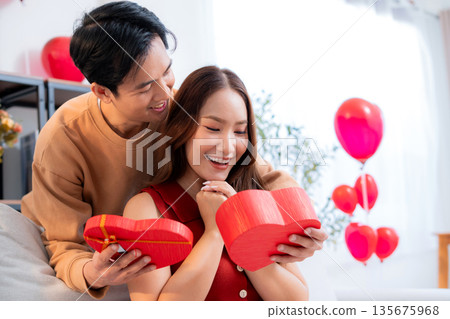 Happy asian man giving heart gift box to girlfriend celebrating Valentine's Day or anniversary. 135675968