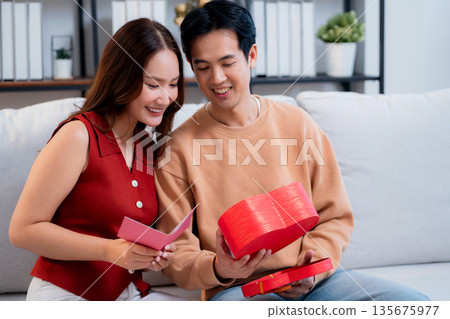 Asian young man and girlfriend celebrating Valentine's Day, woman holding card and gift box. 135675977
