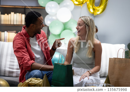 Friends laughing and exchanging gifts at home during festive celebration 135675998