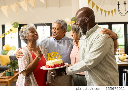 Family celebrating grandmother's 60th birthday with cake and joyful hugs at home 135676011