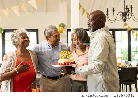 Celebrating birthday, diverse group of seniors smiling with cake in decorated room Celebrating birthday, diverse group of seniors smiling with cake in decorated room 135676012