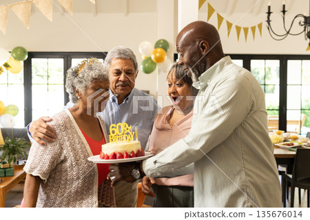 Elderly woman blowing out candles on birthday cake, surrounded by joyful friends Elderly woman blowing out candles on birthday cake, surrounded by joyful friends 135676014