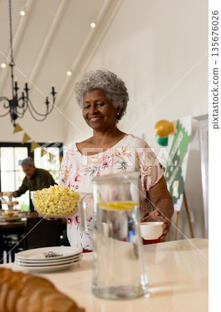Elderly woman holding popcorn and smiling during family celebration at home 135676026