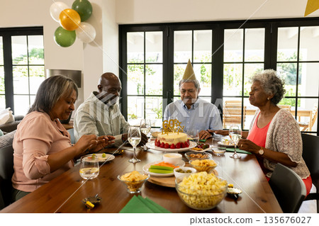 African American family celebrating birthday at home with cake and party hats African American family celebrating birthday at home with cake and party hats 135676027