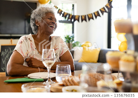 Elderly woman laughing joyfully at home during festive celebration with family Elderly woman laughing joyfully at home during festive celebration with family 135676035