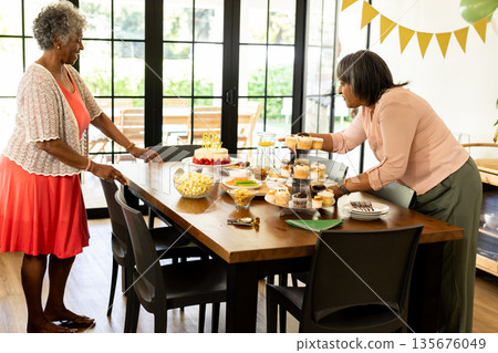 Arranging cupcakes and snacks, African American women preparing for home celebration 135676049